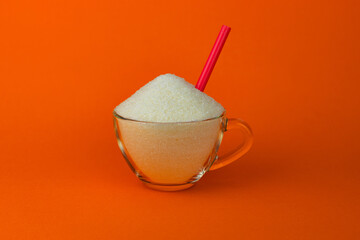 Granulated sugar in a cup with a cocktail tube on an orange background