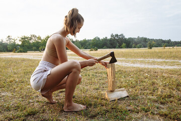 beautiful girl in a camping town chops firewood with an ax for a barbecue