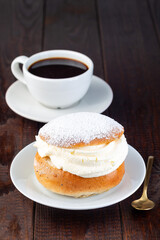 Traditional Swedish dessert Semla or Shrove bun, with almond paste and whipped cream filling, served with cup of coffee, vertical