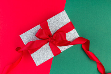 Silver glitter gift box with red ribbon on a red and green paper texture, background for template, horizontal