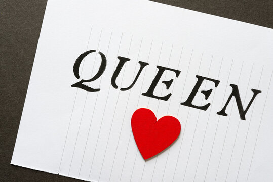 the word queen stencilled in black on note paper (with lines) and a wooden heart hand painted in red