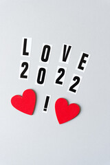 love 2022 with an exclamation mark and two hand painted red hearts on a light gray paper background with copy-space