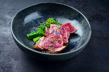 Modern style baby broccoli with fried dry aged sliced beef fillet steak served as close-up on a Nordic design plate