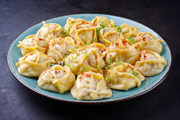 Traditional steamed Kazakh manti garnished with mincemeat and sumah served as close-up on a Nordic design plate with copy space