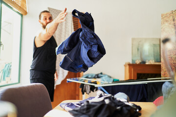 Young bearded man throwing his pants on table after laundry