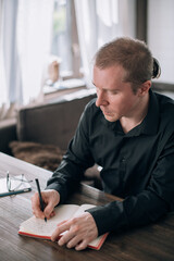 A young man writes in a notebook at the table