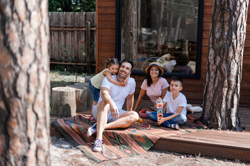 Happy family, two children and their parents, resting near a country house in the woods, enjoying time spent together during summer vacation and holidays