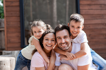 Portrait of a happy family of four, mom, dad, daughter and son, children hug parents, all rejoice in a joint vacation during the hot summer.
