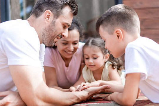 Two adults and two children play palmist, examine each other's hands and palms, lie next to each other and have fun together during the summer weekend