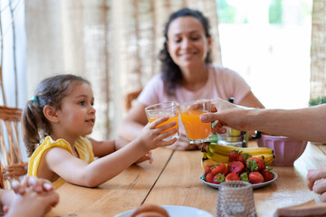 Little girl and her dad clinking glasses with delicious fruit juice, she enjoys breakfast with her beloved family in anticipation of a new interesting summer day.