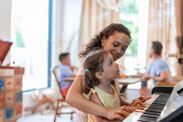 Mom or babysitter teaches a little girl to play the piano, carefully observes the movements of the...