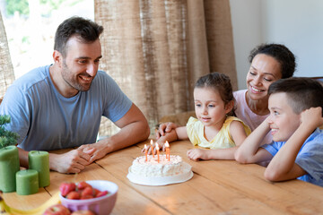 A friendly family celebrates a little girl's sixth birthday at home. The birthday girl is preparing to blow out the birthday candles on the cake.