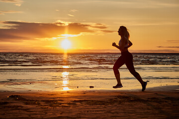 Fototapeta na wymiar Healthy woman runs outdoors during sunset near shore.