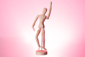 Handmade wooden doll, with raised hand, on a pink background.