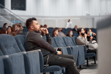 pensive man with a smartphone sitting in lecture hall. - obrazy, fototapety, plakaty