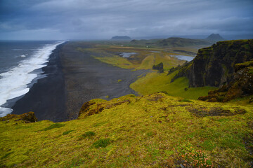 Fototapeta na wymiar A panoramic view of the sweeping black volcanic sand beach and craggy green hills west of Dyrholaey, South Coast of Iceland