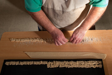 Cocinero masando harina en la mesa para luego cortar la masa con un cuchillo y preparar los bizcochos.