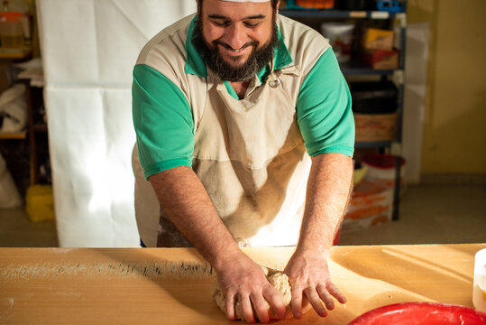 Cocinero masando harina en la mesa para luego cortar la masa con un cuchillo y preparar los bizcochos.