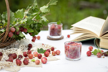 Gooseberry berries on the table with a basket of branches and an open book. Jam in a glass of berries.