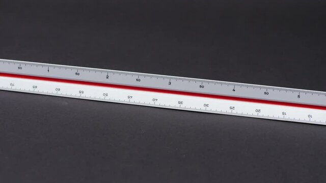 Triangular scale on a dark background. Scale ruler used by architects for measuring and drawing on plans. Engineering equipment in an office. Construction tool for precise drafts.