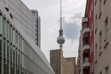 Selective focus view at Berliner Fernsehturm, Television Tower, over buildings from sidewalk on street in Berlin, Germany against overcast sky. © Peeradontax