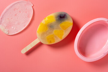 top view homemade milk popsicle mixed with blackberry and blueberry and mango slices and pineapple slices on a pink background