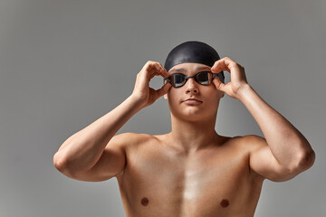 Young male swimmer preparing for the start, close-up portrait of a swimmer in a mask and a hat, gray background, copy space, swimming concept.