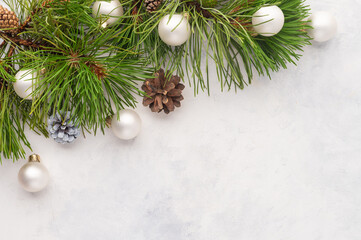 Fototapeta na wymiar A pine branch with cones is decorated with shiny Christmas balls. Simple white background. A beautiful frame for your New Year and Christmas greetings. High angle view.