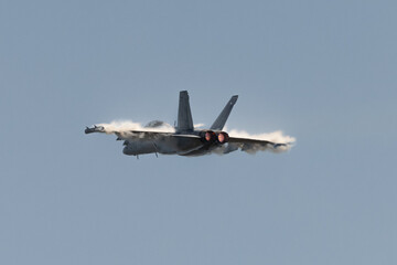 U.S. Navy EA-18G Growler in a high G maneuver, with afterburners on and condensation clouds  over ...