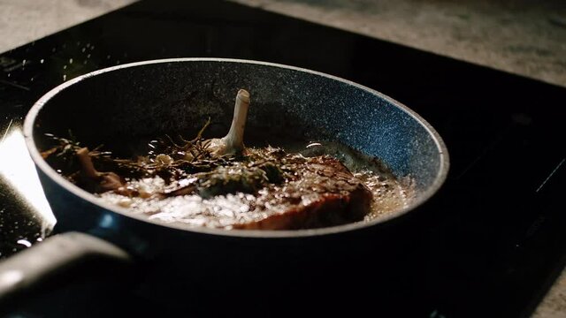 Cooking steak with garlic and rosemary in pan on ceramic stove