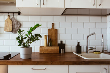 Fototapeta na wymiar Kitchen brass utensils, chef accessories. Hanging kitchen with white tiles wall and wood tabletop.Green plant on kitchen background