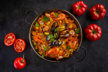Traditional spanish seafood paella with rice, mussels, shrimps in a pan with tomatoes on dark background. view from above, flat lay
