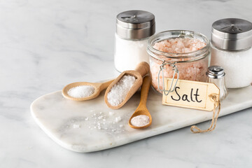 An arrangement of different types of salt on a marble slab including himalayan and kosher salt.