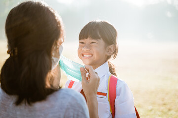 mother help her daughter to put on the mask before going to school