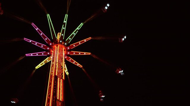 4K multicoloured illuminated tall merry-go-round rotating in night sky. Entertainment, amusement park concept.