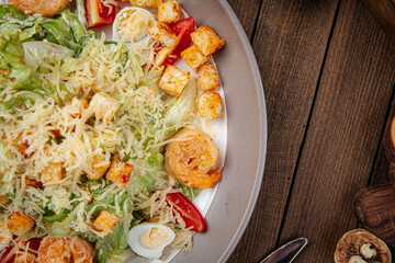 Caesar salad with shrimp and croutons on wooden background