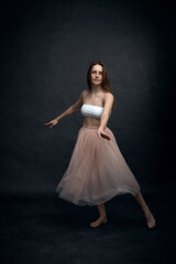 Young girl in white top and peach skirt dancing in black old textured studio