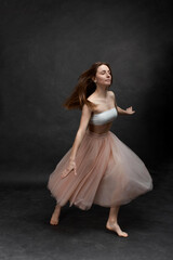 Fototapeta premium Young girl in white top and peach skirt dancing in black old textured studio