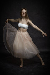 Fototapeta premium Young girl in white top and peach skirt dancing in black old textured studio