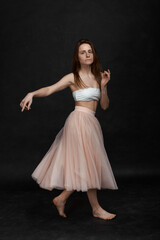 Naklejka premium Young girl in white top and peach skirt dancing in black old textured studio