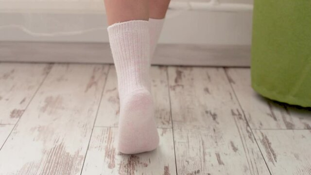 Women's legs. A girl on socks walks up to the window in a short shirt.