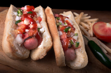 detail of two hot dogs prepared with onion, tomato and chili on a wooden board