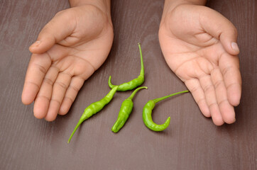 closeup the bunch ripe green chilly hold hand over out of focus brown background.