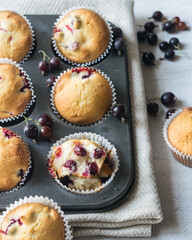 Fresh baked muffins with berries in a muffin tin on grey background, selective focus.