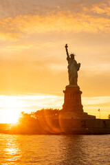 The Statue of Liberty at New York city during sunset with reflections on the ocean © Kenishirotie
