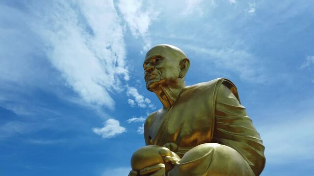 Huge golden statue of monk Luang Pu Thuat, the disciple of lord Buddha in his meditation position against blue sky and cirrocumulus clouds background in Phuttha Utthayan Maharat Ayutthaya Thailand.