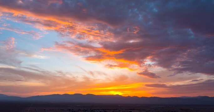 Colorful crimson and golden cloudscape as the sun sets beyond the silhouette of rugged mountains - static time lapse