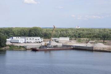 Unloading a barge in a river port, gantry crane unloading crushed stone, river background