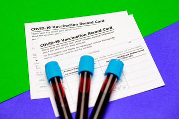 Blood test tubes and covid-19 vaccination record card put across borderline of green and blue...