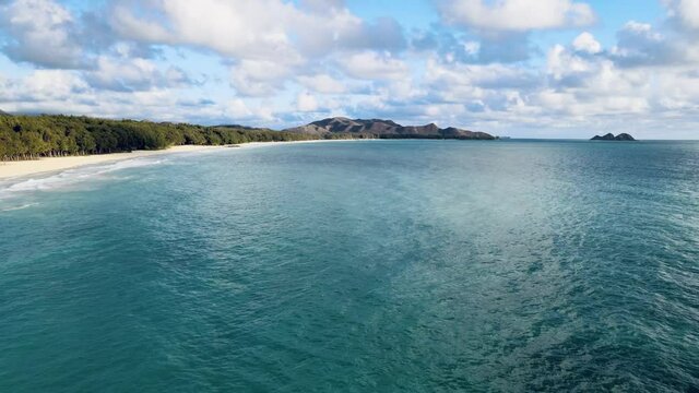 drone video of beautiful lucious water off waimanalo oahu hawaii deep blues of ocean with white sand beach midday sunny tropical paradise with islands off in background panning up to open to view